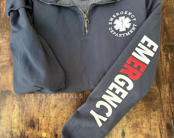 May include: A dark blue sweatshirt with a white zipper and a white and red "Emergency Department" logo on the front. The left sleeve has the word "Emergency" written vertically in white with a red "E".