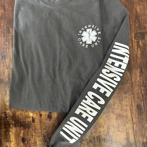 May include: A dark gray long-sleeve shirt with the words "INTENSIVE CARE UNIT" printed in white on the sleeve. The shirt features a white medical symbol and the words "INTENSIVE CARE UNIT" on the chest.
