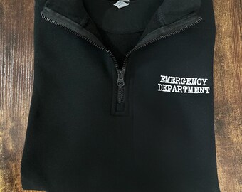 May include: Black quarter-zip sweatshirt with the text "EMERGENCY DEPARTMENT" embroidered in white on the front. The sweatshirt has a zipper that goes up to the collar. The text "ER-ESSENTIALS.COM" is printed on the bottom of the sweatshirt.