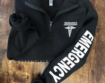 May include: Black quarter-zip sweatshirt with white text on the sleeve that reads "EMERGENCY" and a white graphic on the chest that reads "EMERGENCY DEPARTMENT" with a caduceus symbol.
