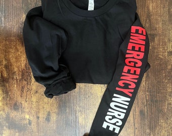 May include: Black long-sleeve shirt with the words "EMERGENCY NURSE" printed vertically on the right sleeve in red and white letters.