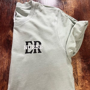 May include: A light green t-shirt with the text "ER NURSE" printed in black letters.