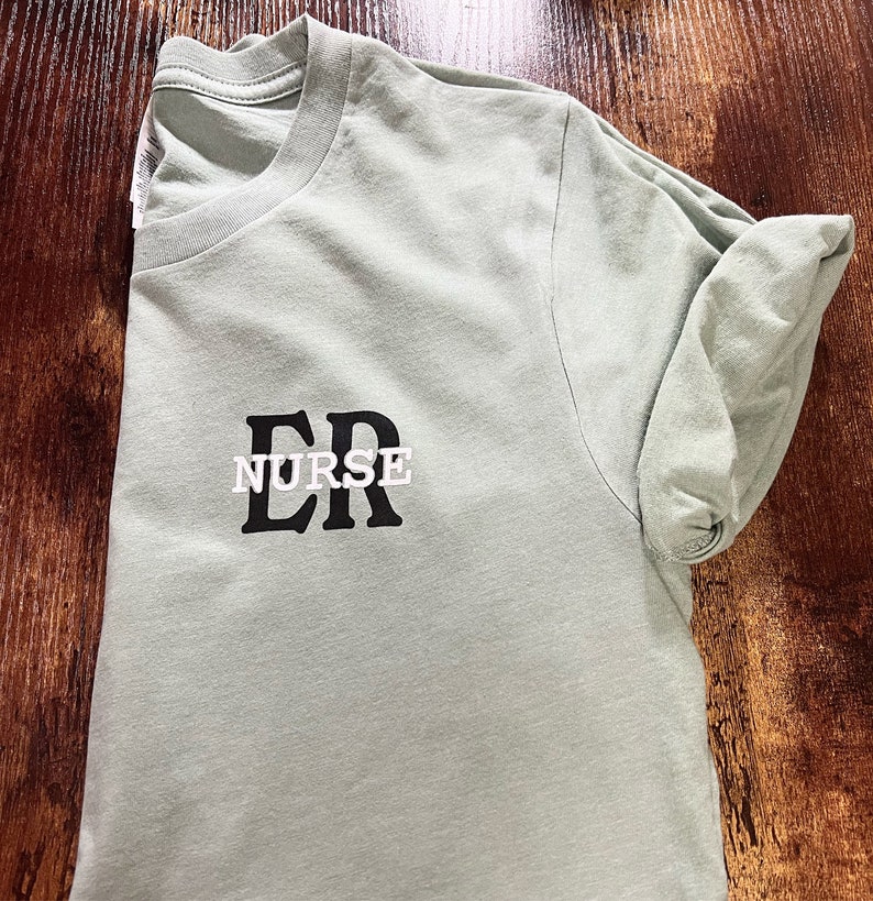 May include: A light green t-shirt with the text "ER NURSE" printed in black letters.
