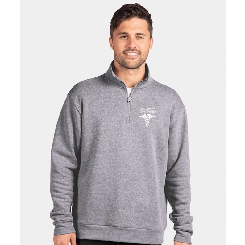 May include: A heather gray 1/4 zip pullover sweatshirt with a white embroidered medical caduceus and the text "Emergency Department".