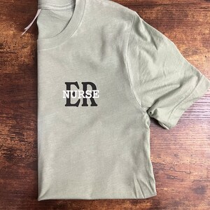 May include: A light green t-shirt with black text that reads "ER NURSE".