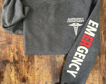 May include: A dark gray sweatshirt with the words "EMERGENCY DEPARTMENT" and a medical symbol on the front. The right sleeve has the word "EMERGENCY" printed vertically in white with the first letter in red.