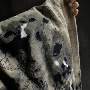 May include: A green fabric with black and white abstract patterns. The fabric has a rough texture and is folded over.