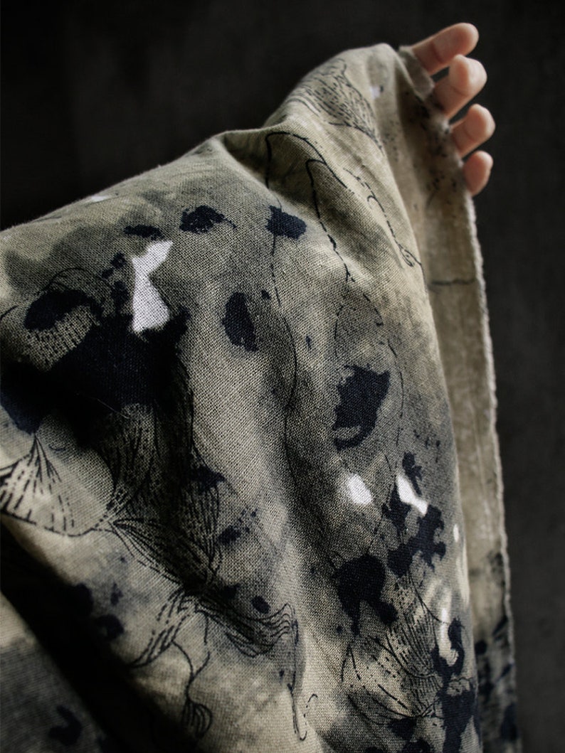 May include: A green fabric with black and white abstract patterns. The fabric has a rough texture and is folded over.