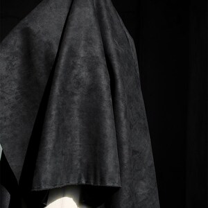 May include: A draped, dark gray fabric with a textured appearance. The fabric is draped over a white mannequin form, creating folds and shadows. The background is a solid black.