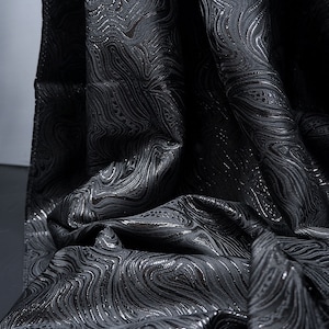 May include: Black fabric with a silver swirl pattern. The fabric is textured and has a subtle sheen.