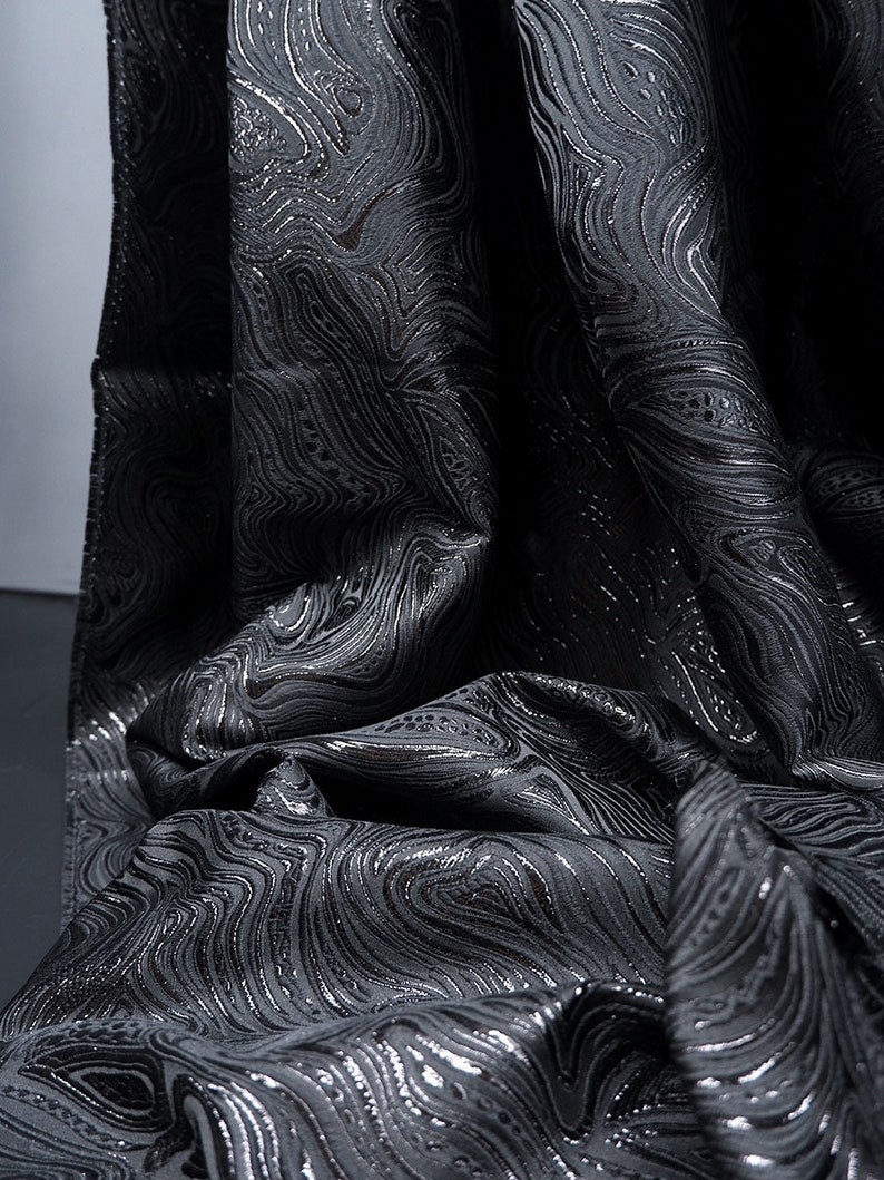 May include: Black fabric with a silver swirl pattern. The fabric is textured and has a subtle sheen.