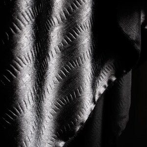 May include: Black fabric with a textured diamond pattern. The fabric is folded and draped, creating a soft, flowing look.