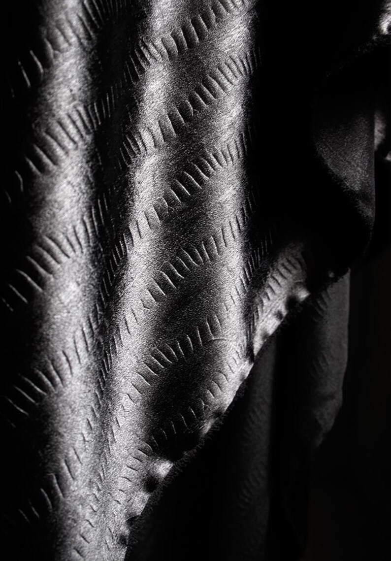 May include: Black fabric with a textured diamond pattern. The fabric is folded and draped, creating a soft, flowing look.