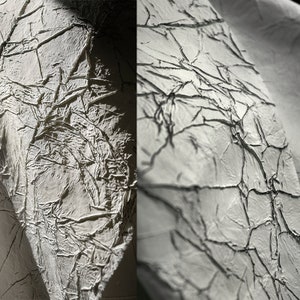 Könnte beinhalten: Nahaufnahme einer weißen, strukturierten Oberfläche mit einem rissigen und faltigen Aussehen. Die Oberfläche hat einen dezenten Glanz und scheint aus einem strapazierfähigen Material zu bestehen.