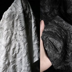 Puede incluir: Dos muestras de tela, una blanca y otra negra, con un patrón texturizado en espiral. La tela tiene un diseño en relieve.