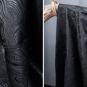 May include: Black fabric with a silver swirl pattern. The fabric is textured and has a subtle sheen.