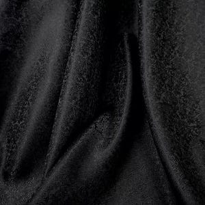 May include: Close-up of a black fabric with a subtle, ornate pattern. The material is draped, creating soft folds and shadows that highlight the intricate design. The fabric has a slight sheen, adding depth to the dark colour.