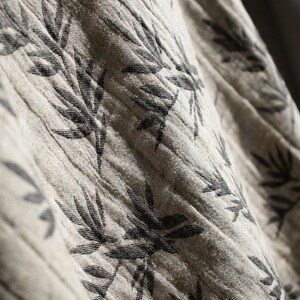 May include: Close-up of a beige fabric with a black leaf pattern. The fabric is textured and has a subtle sheen.