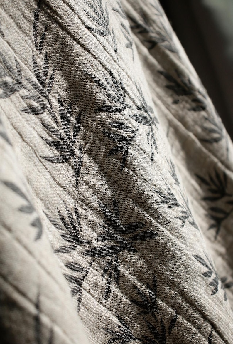 May include: Close-up of a beige fabric with a black leaf pattern. The fabric is textured and has a subtle sheen.