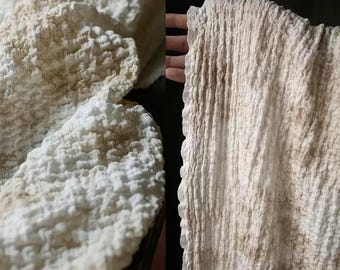 May include: Close-up of textured white fabric with a rough, uneven surface. The fabric has areas of light brown discoloration, creating a natural, aged appearance. The material appears soft and possibly absorbent, suggesting a towel or similar textile.