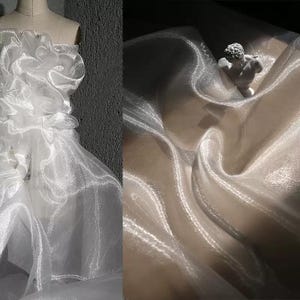 Könnte beinhalten: Ein weißes, trägerloses Kleid mit Rüschendetails auf einer Schaufensterpuppe. Das Kleid besteht aus einem transparenten, schimmernden Stoff. Die rechte Seite des Bildes zeigt eine Nahaufnahme des Stoffes mit einer kleinen Statue im Hintergrund. Der Stoff ist drapiert und fließend.