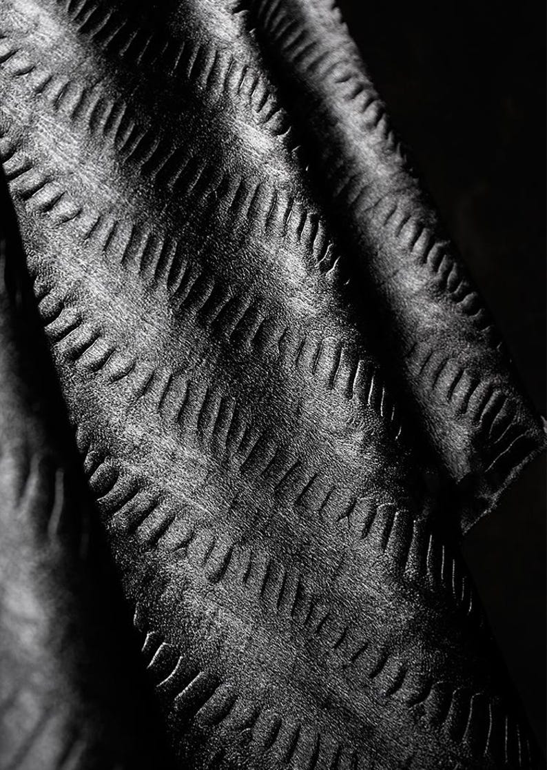 May include: Black fabric with a textured, chevron-like pattern. The fabric is soft and has a subtle sheen.