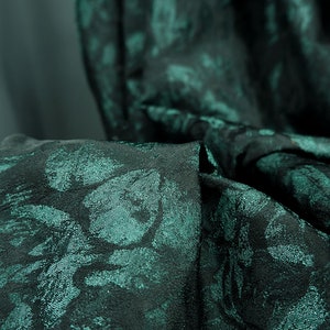 May include: Close-up of a dark green fabric with a subtle floral pattern. The fabric has a textured, almost iridescent sheen.