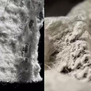 May include: Close-up of white lace fabric with a delicate, intricate pattern. The fabric is soft and textured, with a slightly frayed edge.