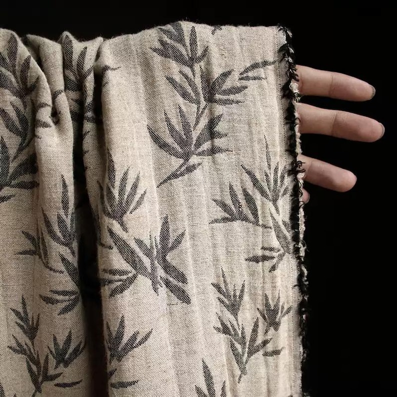 May include: Beige fabric with a black leaf pattern. The fabric has a raw edge.