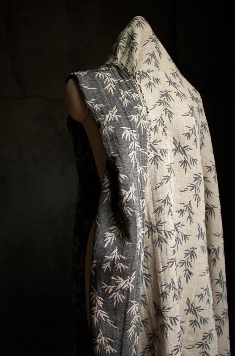 May include: A black and white fabric with a bamboo leaf pattern. The fabric is draped over a dress form.