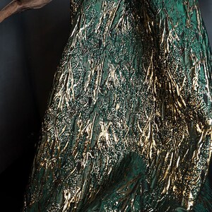 May include: Green fabric with a gold metallic pattern. The fabric has a textured, woven look.