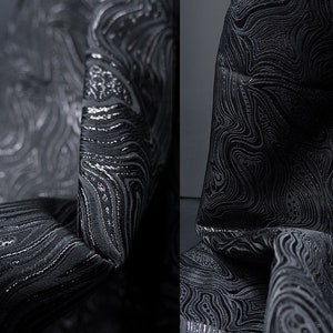 May include: Black fabric with a silver metallic swirl pattern. The fabric is textured and has a subtle sheen.