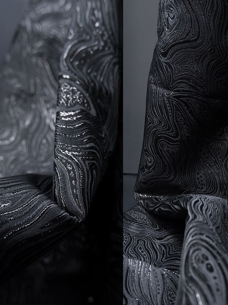 May include: Black fabric with a silver metallic swirl pattern. The fabric is textured and has a subtle sheen.