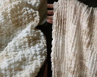 May include: White fabric with a textured, crinkled surface. The fabric has a subtle brown and beige color variation.