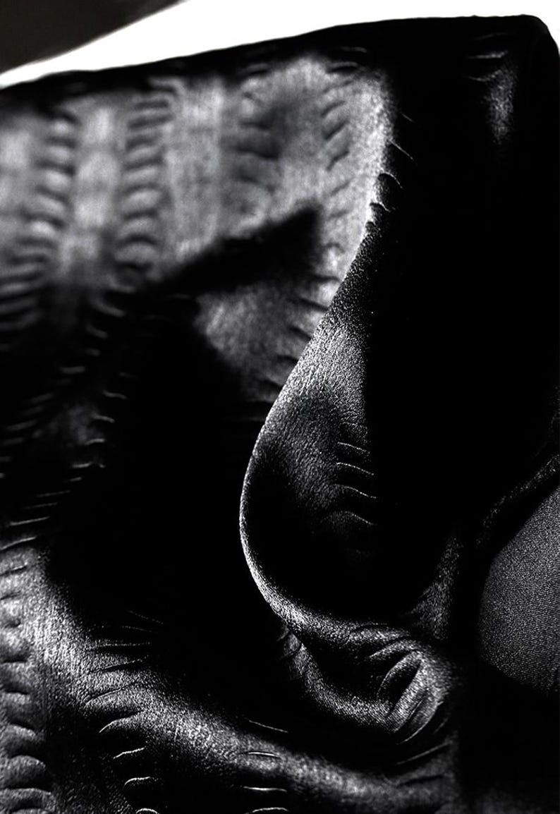 May include: Black fabric with a textured, embossed pattern. The fabric is folded and draped, creating a soft, flowing look.