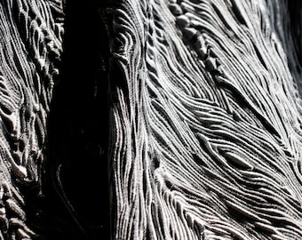 May include: Close-up of a textured fabric with a wavy, rippled pattern. The fabric is a dark gray color and appears to be made of a soft, pliable material.