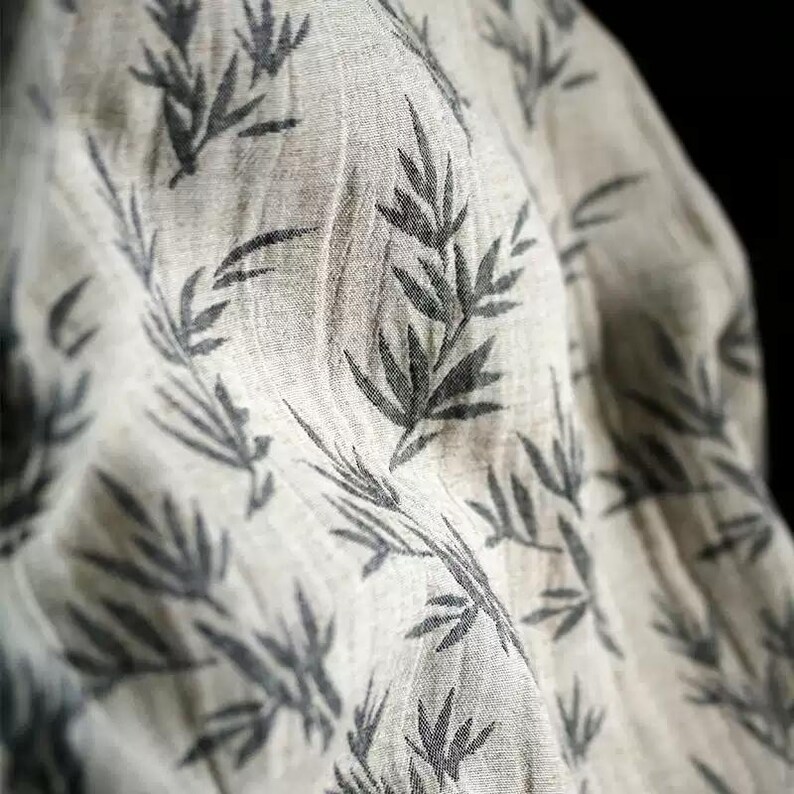 May include: A close-up of a white fabric with a black leaf pattern. The fabric is soft and textured, and the leaves are printed in a repeating pattern.