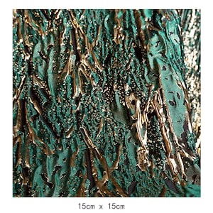 May include: Green and gold fabric with a textured, embossed pattern. The fabric has a metallic sheen and a raised design that resembles branches or vines.