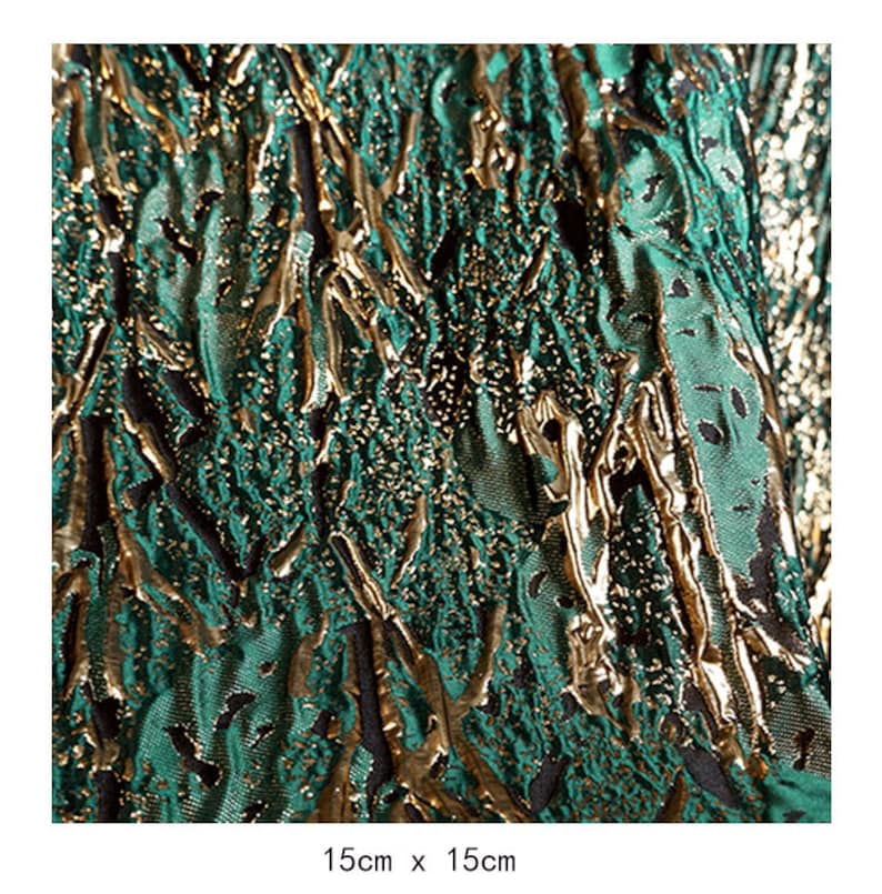 May include: Green and gold fabric with a textured, embossed pattern. The fabric has a metallic sheen and a raised design that resembles branches or vines.