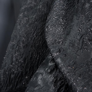 May include: Black fabric with a textured, embossed pattern. The fabric has a subtle sheen and a slightly rough texture.