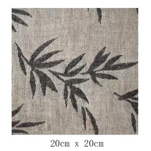 May include: A close-up of a beige fabric with a black leaf pattern. The fabric is textured and has a subtle sheen. The leaves are stylized and have a slightly abstract look. The fabric is 20 inches by 20 inches.
