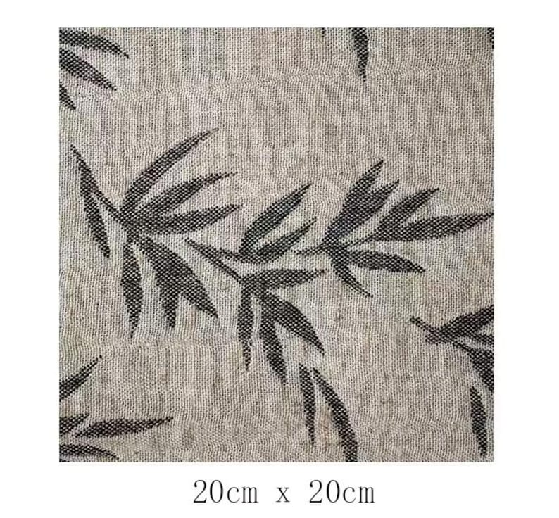 May include: A close-up of a beige fabric with a black leaf pattern. The fabric is textured and has a subtle sheen. The leaves are stylized and have a slightly abstract look. The fabric is 20 inches by 20 inches.