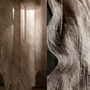 Puede incluir: Primer plano de una tela beige transparente con un aspecto texturizado y arrugado. La tela está drapeada, con luz filtrándose, creando sombras y resaltando el patrón tejido. La tela tiene una estética natural y orgánica.