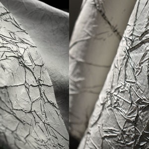 May include: Close-up of a white fabric with a textured, cracked surface. The fabric is folded and draped, creating a dramatic effect.