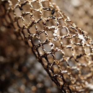 Könnte beinhalten: Nahaufnahme eines braunen und weißen gewebten Netzstoffes mit einem schwarzen Faden, der durch ihn verläuft.