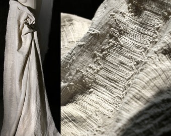 May include: A close-up of a white linen fabric with a textured woven pattern. The fabric is draped over a form and has a soft, natural look.