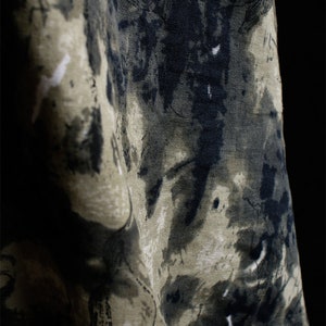 May include: A close-up of a fabric with a dark green and black abstract pattern. The fabric has a textured surface and a slightly faded look.