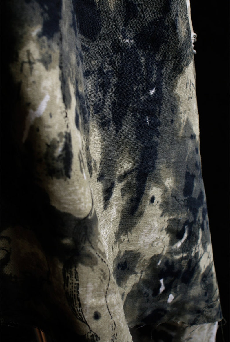 May include: A close-up of a fabric with a dark green and black abstract pattern. The fabric has a textured surface and a slightly faded look.