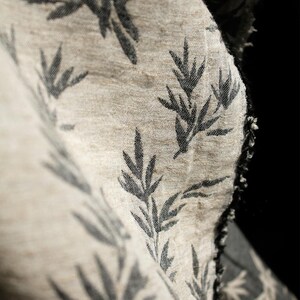 May include: A close-up of a beige fabric with a black leaf pattern. The fabric is textured and has a raw edge.