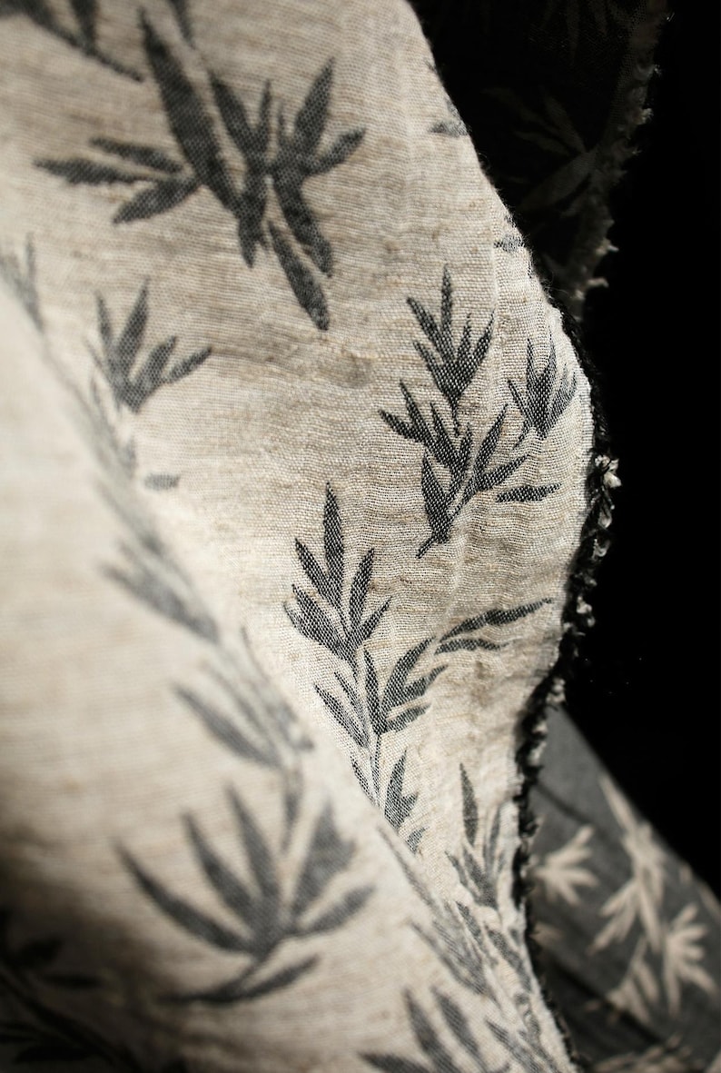 May include: A close-up of a beige fabric with a black leaf pattern. The fabric is textured and has a raw edge.